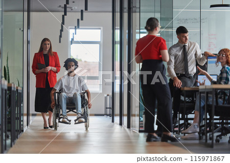 A group of young business people in a modern glass-walled office captures the essence of diversity and collaboration, while two colleagues, including an African American businessman in a wheelchair 115971867