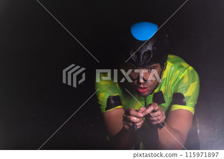 A triathlete braving the rain as he cycles through the night, preparing himself for the upcoming marathon. The blurred raindrops in the foreground and the dark, moody atmosphere in the background add A triathlete braving the rain as he cycles through the night, preparing himself for the upcoming marathon. The blurred raindrops in the foreground and the dark, moody atmosphere in the background add 115971897