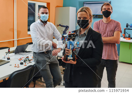 A group of colleagues working together in a robotics laboratory, focusing on the intricate fields of robotics and 3D printing. Showcase their dedication to innovation, as they engage in research 115971934