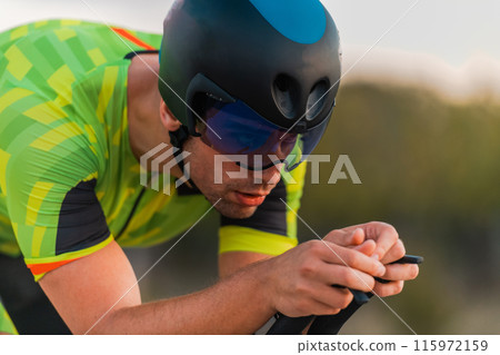 Close up photo of triathlete riding his bicycle during sunset, preparing for a marathon. The warm colors of the sky provide a beautiful backdrop for his determined and focused effort. 115972159