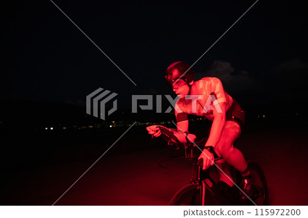 A triathlete rides his bike in the darkness of night, pushing himself to prepare for a marathon. The contrast between the darkness and the light of his bike creates a sense of drama and highlights the A triathlete rides his bike in the darkness of night, pushing himself to prepare for a marathon. The contrast between the darkness and the light of his bike creates a sense of drama and highlights the 115972200