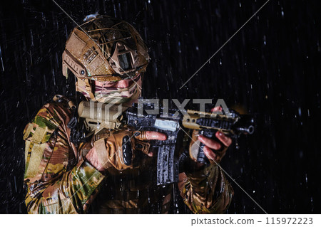 Army soldier in Combat Uniforms with an assault rifle, plate carrier and combat helmet going on a dangerous mission on a rainy night. 115972223