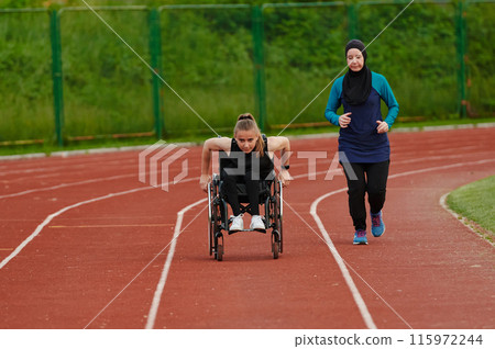 A Muslim woman in a burqa running together with a woman in a wheelchair on the marathon course, preparing for future competitions. 115972244