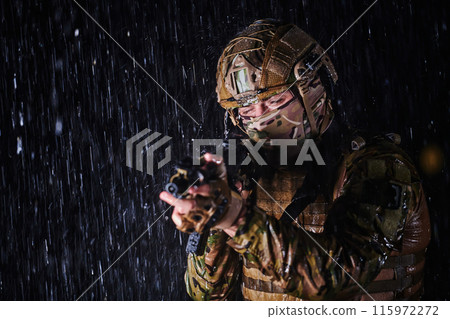 Army soldier in Combat Uniforms with an assault rifle, plate carrier and combat helmet going on a dangerous mission on a rainy night. Army soldier in Combat Uniforms with an assault rifle, plate carrier and combat helmet going on a dangerous mission on a rainy night. 115972272