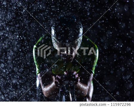 A triathlete braving the rain as he cycles through the night, preparing himself for the upcoming marathon. The blurred raindrops in the foreground and the dark, moody atmosphere in the background add 115972296