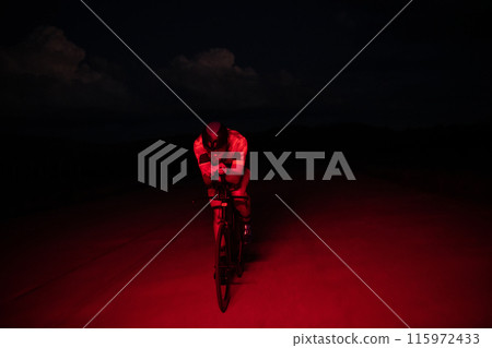 A triathlete rides his bike in the darkness of night, pushing himself to prepare for a marathon. The contrast between the darkness and the light of his bike creates a sense of drama and highlights the A triathlete rides his bike in the darkness of night, pushing himself to prepare for a marathon. The contrast between the darkness and the light of his bike creates a sense of drama and highlights the 115972433