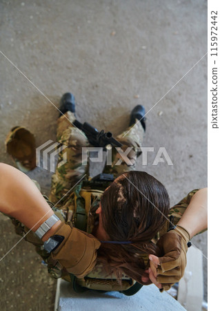 A woman in a professional military uniform sits in an abandoned building, ready for a dangerous mission, exuding bravery and determination 115972442