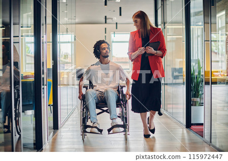 A group of young business people in a modern glass-walled office captures the essence of diversity and collaboration, while two colleagues, including an African American businessman in a wheelchair A group of young business people in a modern glass-walled office captures the essence of diversity and collaboration, while two colleagues, including an African American businessman in a wheelchair 115972447