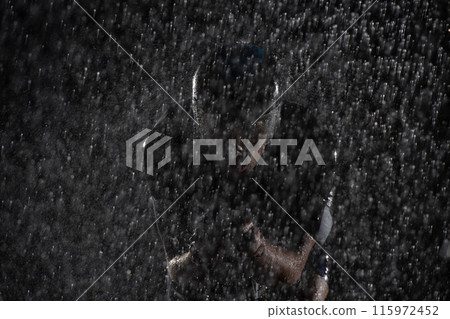 A triathlete braving the rain as he cycles through the night, preparing himself for the upcoming marathon. The blurred raindrops in the foreground and the dark, moody atmosphere in the background add A triathlete braving the rain as he cycles through the night, preparing himself for the upcoming marathon. The blurred raindrops in the foreground and the dark, moody atmosphere in the background add 115972452