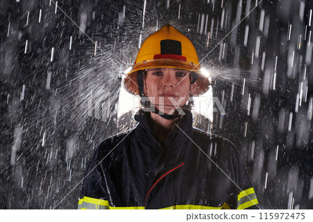 A determined female firefighter in a professional uniform striding through the dangerous, rainy night on a daring rescue mission, showcasing her unwavering bravery and commitment to saving lives. 115972475