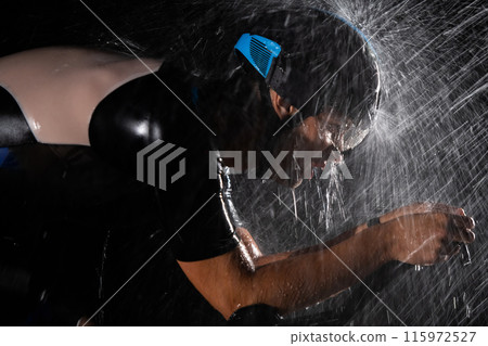 A triathlete braving the rain as he cycles through the night, preparing himself for the upcoming marathon. The blurred raindrops in the foreground and the dark, moody atmosphere in the background add A triathlete braving the rain as he cycles through the night, preparing himself for the upcoming marathon. The blurred raindrops in the foreground and the dark, moody atmosphere in the background add 115972527