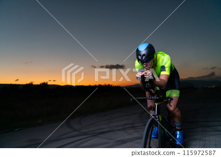 A triathlete rides his bike in the darkness of night, pushing himself to prepare for a marathon. The contrast between the darkness and the light of his bike creates a sense of drama and highlights the A triathlete rides his bike in the darkness of night, pushing himself to prepare for a marathon. The contrast between the darkness and the light of his bike creates a sense of drama and highlights the 115972587