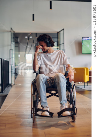 A sad businessman in a wheelchair occupies a hallway within a modern startup coworking center, embodying inclusivity and determination in the business environment 115972603