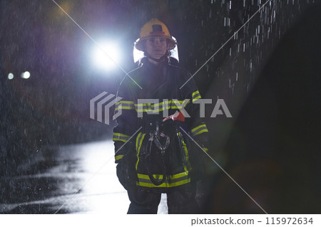 A determined female firefighter in a professional uniform striding through the dangerous, rainy night on a daring rescue mission, showcasing her unwavering bravery and commitment to saving lives. 115972634