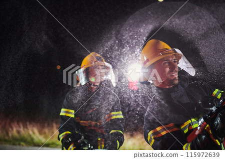 Firefighters using a water hose to eliminate a fire hazard. Team of female and male firemen in dangerous rescue mission.  115972639