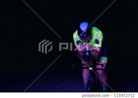A triathlete rides his bike in the darkness of night, pushing himself to prepare for a marathon. The contrast between the darkness and the light of his bike creates a sense of drama and highlights the 115972712