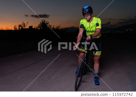 A triathlete rides his bike in the darkness of night, pushing himself to prepare for a marathon. The contrast between the darkness and the light of his bike creates a sense of drama and highlights the 115972742