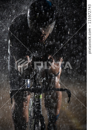 A triathlete braving the rain as he cycles through the night, preparing himself for the upcoming marathon. The blurred raindrops in the foreground and the dark, moody atmosphere in the background add A triathlete braving the rain as he cycles through the night, preparing himself for the upcoming marathon. The blurred raindrops in the foreground and the dark, moody atmosphere in the background add 115972743