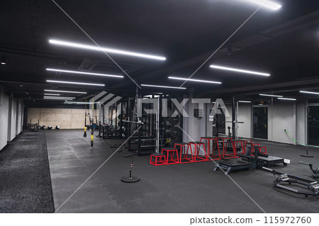 An empty modern gymnasium with a variety of equipment, offering a spacious, functional, and well-equipped training facility for workouts, fitness, and strength training 115972760