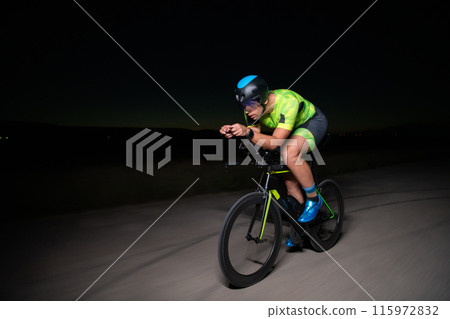 A triathlete rides his bike in the darkness of night, pushing himself to prepare for a marathon. The contrast between the darkness and the light of his bike creates a sense of drama and highlights the A triathlete rides his bike in the darkness of night, pushing himself to prepare for a marathon. The contrast between the darkness and the light of his bike creates a sense of drama and highlights the 115972832