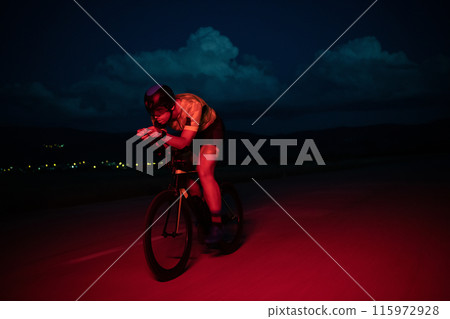 A triathlete rides his bike in the darkness of night, pushing himself to prepare for a marathon. The contrast between the darkness and the light of his bike creates a sense of drama and highlights the 115972928