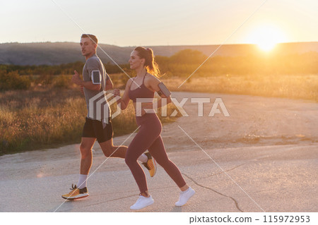 A handsome young couple running together during the early morning hours, with the mesmerizing sunrise casting a warm glow, symbolizing their shared love and vitality A handsome young couple running together during the early morning hours, with the mesmerizing sunrise casting a warm glow, symbolizing their shared love and vitality 115972953