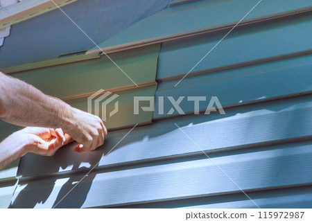 Workers install vinyl plastic siding panels on wall facade of new home during construction 115972987