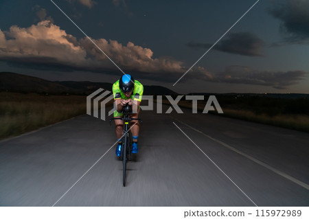 A triathlete rides his bike in the darkness of night, pushing himself to prepare for a marathon. The contrast between the darkness and the light of his bike creates a sense of drama and highlights the 115972989