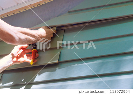 Worker installing vinyl plastic siding panels on wall facade of new house during construction 115972994