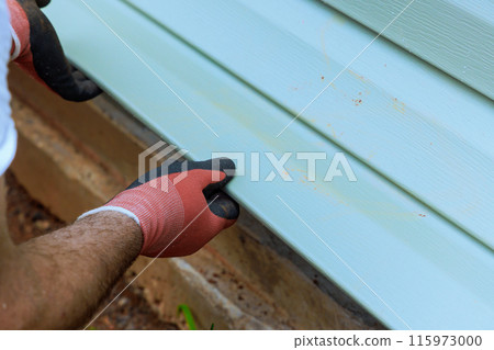 During construction, worker installs vinyl plastic siding on wall facade of new home 115973000
