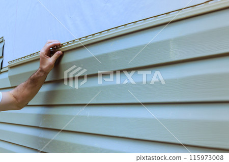 An experienced contractor installs vinyl siding plastic panels on facade wall of new home 115973008