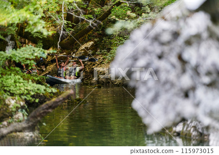 A young couple enjoying an idyllic kayak ride in the middle of a beautiful river surrounded by forest greenery 115973015