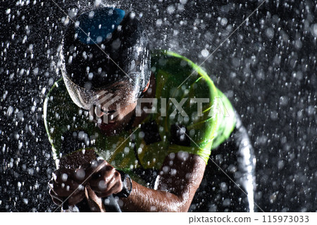 A triathlete braving the rain as he cycles through the night, preparing himself for the upcoming marathon. The blurred raindrops in the foreground and the dark, moody atmosphere in the background add 115973033