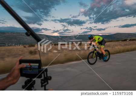 A videographer recording a triathlete riding his bike preparing for an upcoming marathon.Athlete's physical endurance and the dedication required to succeed in the sport. 115973108