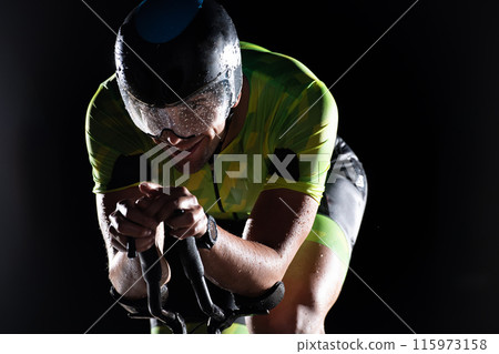 A triathlete rides his bike in the darkness of night, pushing himself to prepare for a marathon. The contrast between the darkness and the light of his bike creates a sense of drama and highlights the A triathlete rides his bike in the darkness of night, pushing himself to prepare for a marathon. The contrast between the darkness and the light of his bike creates a sense of drama and highlights the 115973158