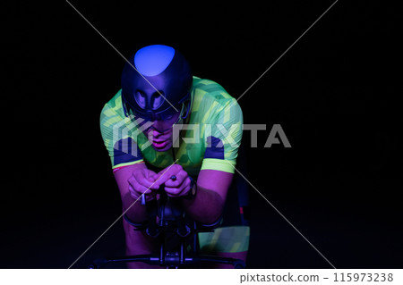 A triathlete rides his bike in the darkness of night, pushing himself to prepare for a marathon. The contrast between the darkness and the light of his bike creates a sense of drama and highlights the A triathlete rides his bike in the darkness of night, pushing himself to prepare for a marathon. The contrast between the darkness and the light of his bike creates a sense of drama and highlights the 115973238