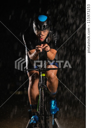 A triathlete braving the rain as he cycles through the night, preparing himself for the upcoming marathon A triathlete braving the rain as he cycles through the night, preparing himself for the upcoming marathon 115973253
