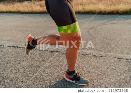 Closeup of muscular legs of a triathlete in professional equipment running early in the morning, preparing for a marathon, dedication to sports and readiness for marathon challenges 115973268