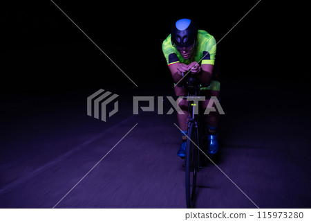 A triathlete rides his bike in the darkness of night, pushing himself to prepare for a marathon. The contrast between the darkness and the light of his bike creates a sense of drama and highlights the 115973280