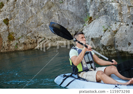 A young man kayaking and exploring a river, surrounded by an impressive natural scenery that exudes an adventurous spirit A young man kayaking and exploring a river, surrounded by an impressive natural scenery that exudes an adventurous spirit 115973298