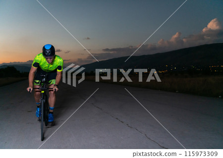 A triathlete rides his bike in the darkness of night, pushing himself to prepare for a marathon. The contrast between the darkness and the light of his bike creates a sense of drama and highlights the A triathlete rides his bike in the darkness of night, pushing himself to prepare for a marathon. The contrast between the darkness and the light of his bike creates a sense of drama and highlights the 115973309