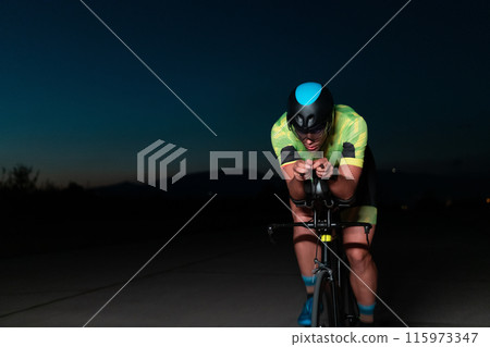 A triathlete rides his bike in the darkness of night, pushing himself to prepare for a marathon. The contrast between the darkness and the light of his bike creates a sense of drama and highlights the 115973347