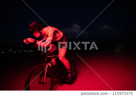 A triathlete rides his bike in the darkness of night, pushing himself to prepare for a marathon. The contrast between the darkness and the light of his bike creates a sense of drama and highlights the 115973375