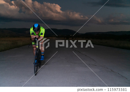 A triathlete rides his bike in the darkness of night, pushing himself to prepare for a marathon. The contrast between the darkness and the light of his bike creates a sense of drama and highlights the A triathlete rides his bike in the darkness of night, pushing himself to prepare for a marathon. The contrast between the darkness and the light of his bike creates a sense of drama and highlights the 115973381