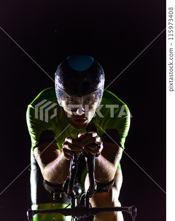 A triathlete rides his bike in the darkness of night, pushing himself to prepare for a marathon. The contrast between the darkness and the light of his bike creates a sense of drama and highlights the 115973408