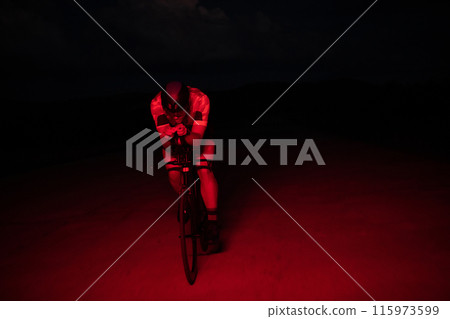 A triathlete rides his bike in the darkness of night, pushing himself to prepare for a marathon. The contrast between the darkness and the light of his bike creates a sense of drama and highlights the 115973599