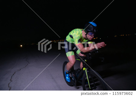 A triathlete rides his bike in the darkness of night, pushing himself to prepare for a marathon. The contrast between the darkness and the light of his bike creates a sense of drama and highlights the 115973602