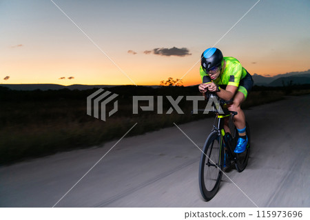 A triathlete rides his bike in the darkness of night, pushing himself to prepare for a marathon. The contrast between the darkness and the light of his bike creates a sense of drama and highlights the A triathlete rides his bike in the darkness of night, pushing himself to prepare for a marathon. The contrast between the darkness and the light of his bike creates a sense of drama and highlights the 115973696