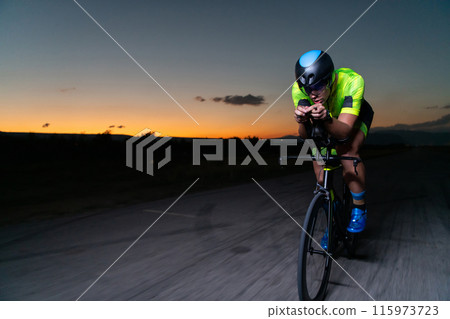 A triathlete rides his bike in the darkness of night, pushing himself to prepare for a marathon. The contrast between the darkness and the light of his bike creates a sense of drama and highlights the A triathlete rides his bike in the darkness of night, pushing himself to prepare for a marathon. The contrast between the darkness and the light of his bike creates a sense of drama and highlights the 115973723