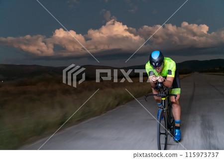 A triathlete rides his bike in the darkness of night, pushing himself to prepare for a marathon. The contrast between the darkness and the light of his bike creates a sense of drama and highlights the A triathlete rides his bike in the darkness of night, pushing himself to prepare for a marathon. The contrast between the darkness and the light of his bike creates a sense of drama and highlights the 115973737